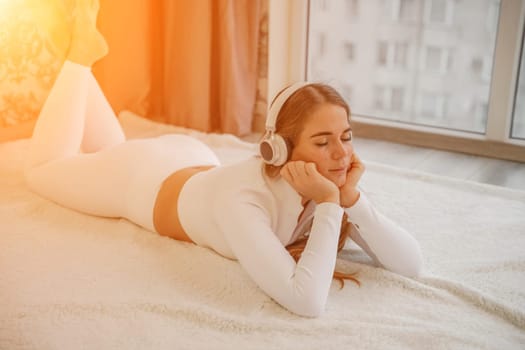 Top view portrait of relaxed woman listening to music with headphones lying on carpet at home. She is dressed in a White tracksuit