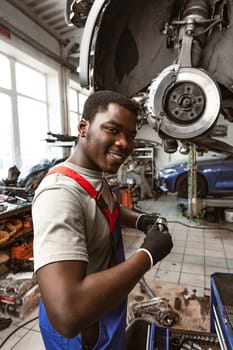 African male auto-mechanic repairing car brakes under the car in auto service close up