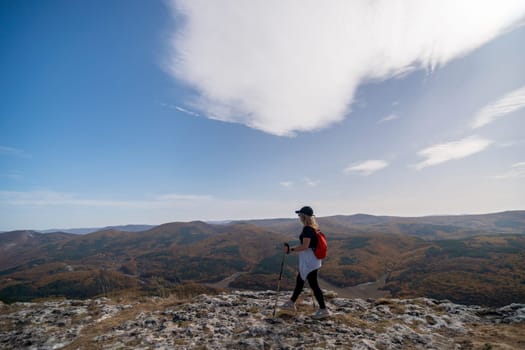 woman on mountain peak looking in beautiful mountain valley in autumn. Landscape with sporty young woman, blu sky in fall. Hiking. Nature.