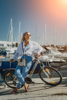 Woman enjoys bike ride along waterfront, Marina surroundings. She is wearing a white shirt and blue jeans, and she has a handbag with her. Capturing outdoor bike ride by waterfront