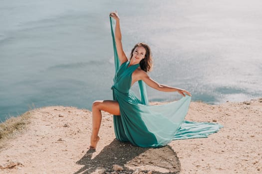 Woman green dress sea. Female dancer posing on a rocky outcrop high above the sea. Girl on the nature on blue sky background. Fashion photo