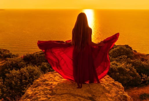 Woman sunset sea red dress, side view a happy beautiful sensual woman in a red long dress posing on a rock high above the sea on sunset