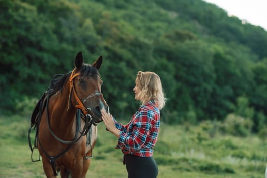 Happy blonde with horse in forest. Woman and a horse walking through the field during the day. Dressed in a plaid shirt and black leggings