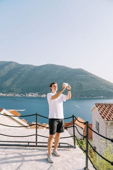 Young man takes pictures with his phone while standing on an observation deck by the sea. High quality photo