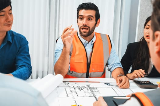 Diverse group of civil engineer and client working together on architectural project, reviewing construction plan and building blueprint at meeting table. Prudent