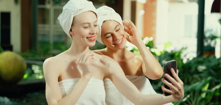 Couple of young beautiful women with beautiful skin in white towel taking a photo together at outdoor surrounded by peaceful natural environment. Beauty and healthy spa concept. Tranquility.