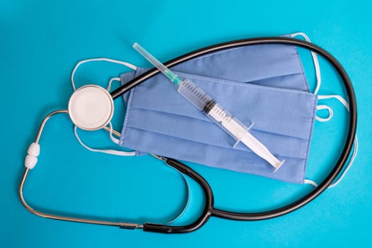 Two blue cotton medical masks, stethoscope and syringe on blue background close up