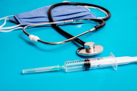 Two blue cotton medical masks, stethoscope and syringe on blue background close up