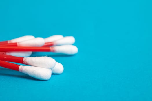 A pile of red cotton buds on a blue background close up, copy space