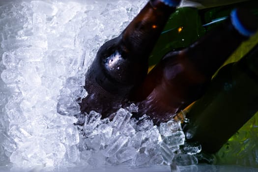 Bucket with bottles of beer and ice cubes, top view. Cubes of ice and colorful bottles with cold beer and drinks. Top view, close-up. Preparation for the festive event.