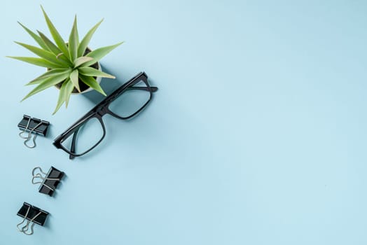 Top view of Glasses and black binder paper clip on blue table