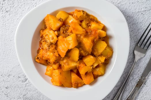 Minced meat and potato dish on white porcelain plate on stone table