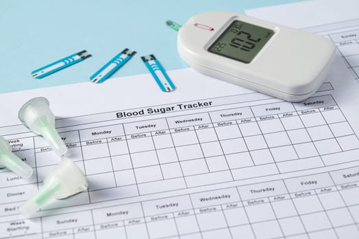 Top view of glucometer, lancet pen, strips and blood sugar tracker on blue background. diabetes test kit