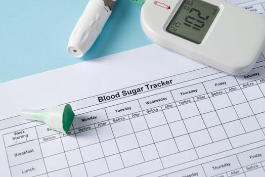 Top view of glucometer, lancet pen, strips and blood sugar tracker on blue background. diabetes test kit