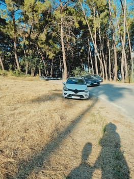 vertical photo of a white car parked near the road coming out of the forest. concept of traveling by car, summer vacation, car trip