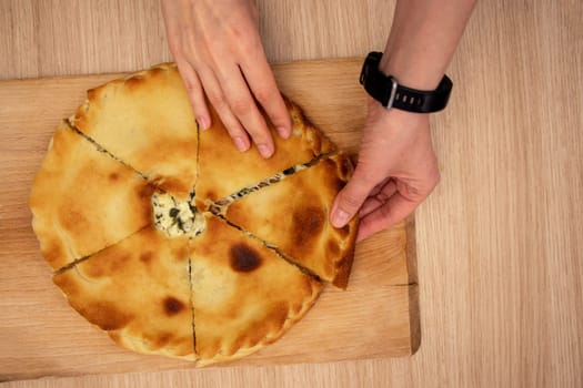 top view of female hands taking a piece of pie lying on a wooden board. Ossetian pie. flat lay