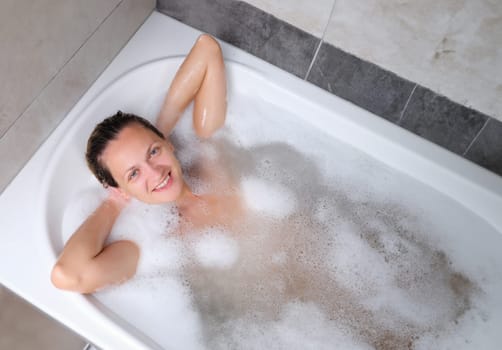 Beautiful young smiling woman lies in bath. Relaxing in bathroom at wellness centre.