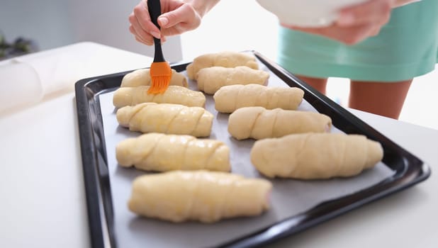 Woman prepares croissants and brush dough with egg yolk. Sweet puff pastry and making traditional French croissant