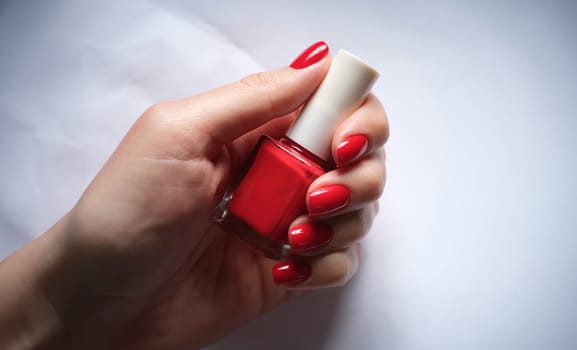 Female nails holds bottle of bright red nail polish. Beautiful manicure concept