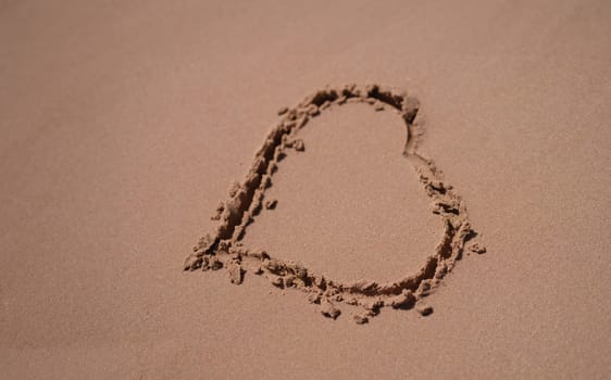 Seashore with sand and hearts. Ocean coast and beach coast. Drawing of a heart on sandy beach with sunlight.