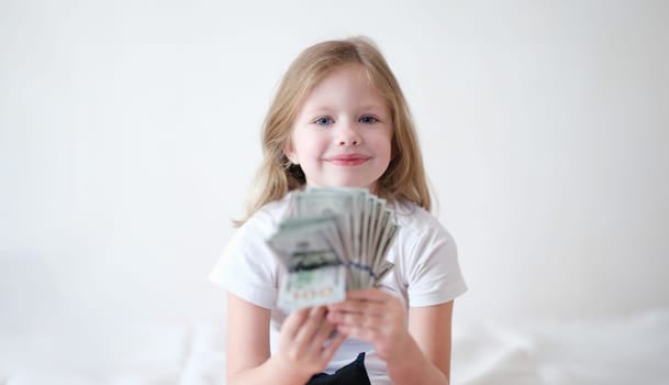Smiling beautiful little girl is holding fan of dollars. Child success and financial income concept