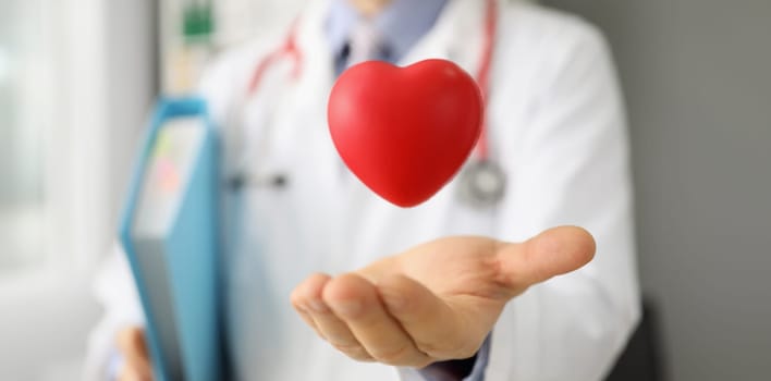 Close-up of cardiologist throw red plastic heart and catch it in palm, save life through donation or charity activity. Medicine, cardiology, health concept