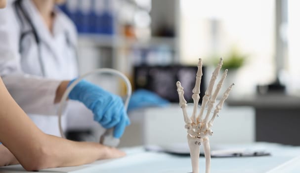 Close-up of doctor do ultrasound of hand, skeleton hand model on desk, medical anatomy science. Medicine, biology, lab, healthcare, injury, clinic concept