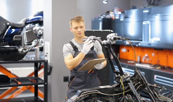 Portrait of maintenance service worker in uniform examine motorbike, man with clipboard paper. Pit stop, garage, high quality help, fixing station concept