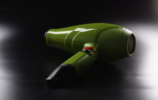 Close-up of green hairdryer, brand new device lay on dark background, instrument for beauty master. Last model to dry hair. Barbershop, technology concept