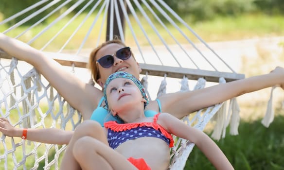 Portrait of mother and daughter lay on hammock in shade, enjoy life, time with family, mother daughter time. Chilling, traveling, relax, parenthood concept