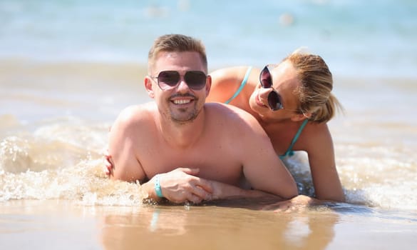 Portrait of smiling couple laying on coastline, posing for memorable picture from vacation. Middle aged man and pretty woman in sunglasses. Love concept