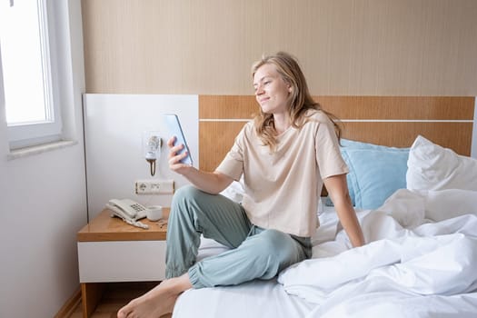 Woman using smartphone lying in bed at hotel room