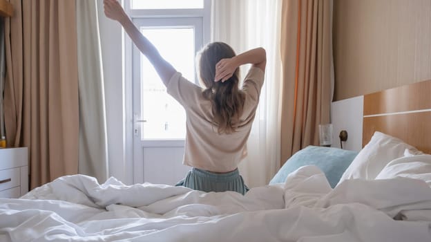 Woman stretching in bed after wake up, back view, sun shines from the window