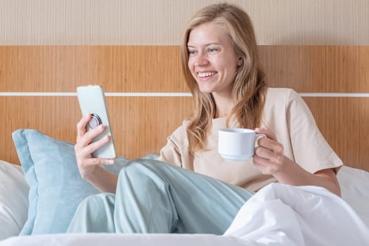 Woman stretching in bed after wake up and having coffee , sun shines from the window