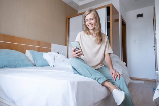 Woman using smartphone and laughing sitting in bed at hotel room