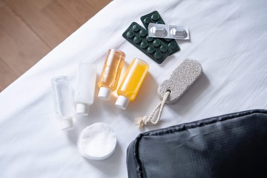 Travel cosmetics kit with bottles, pills and cosmetics on bed , top view