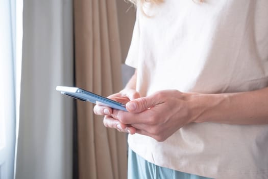 closeup of unrecognizable person in home clothes using phone standing by the window in hotel room