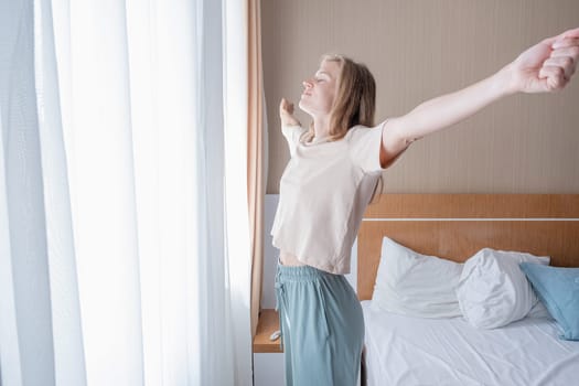 woman waking up and stretching in the morning in hotel room by the window