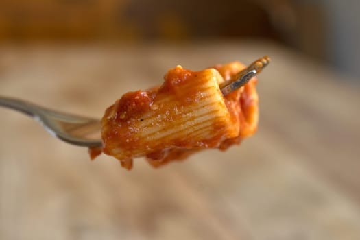 fork with rigatoni with tomato sauce and in the background a plate of pasta with sauce