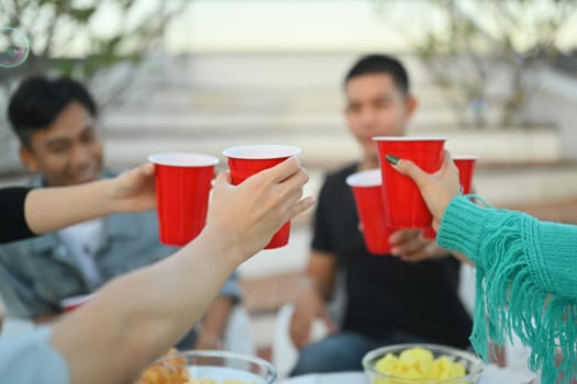 Friendship and celebration and lifestyle concept. Group of adult friends clinking plastic cups on rooftop party.