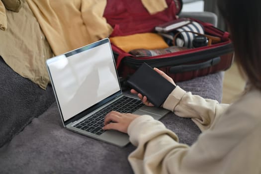 Cropped shot of woman hand holding a passport and typing on laptop, booking tickets or hotel room.