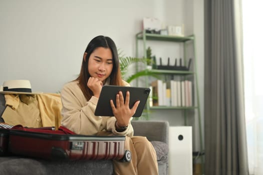 Pretty young Asian woman planning for trip with laptop, getting ready for holidays travel trip in living room