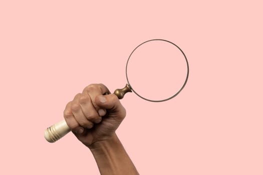 Black male hand holding vintage magnifying loupe on pink background. High quality photo