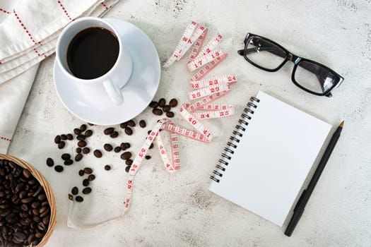 Cup of coffee and coffee beans background with measure tap and notebook on white desk. Beverage and diet concept. Directly above. Flat lay. Copy space.