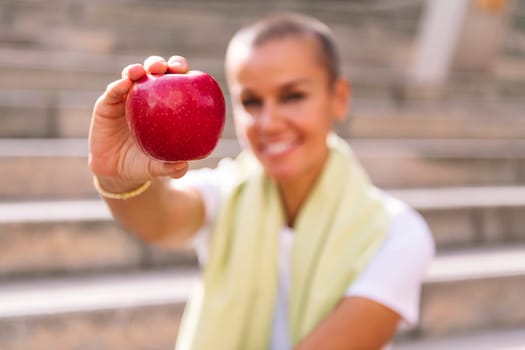 young sports woman showing an apple after workout, concept of healthy and active lifestyle, selective focus on the apple