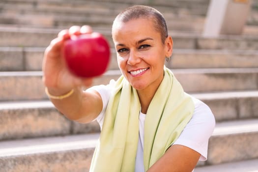 young sports woman showing an apple after workout, concept of healthy and active lifestyle, focus on the smiling face