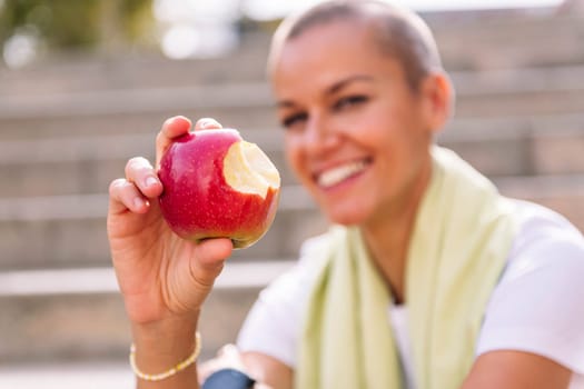 smiling sports woman showing a bitten apple after workout, concept of healthy and active lifestyle, focus on the apple