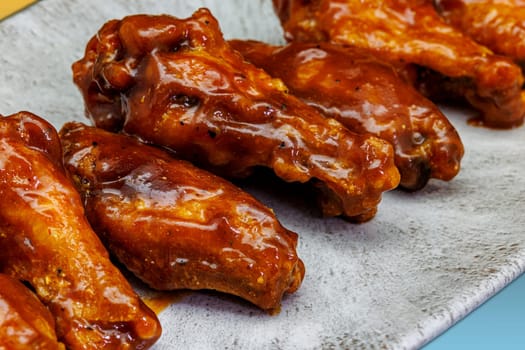 Composition of a plate of chicken wings with BBQ sauce on a yellow and light blue gradient background