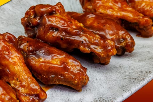 Composition of a plate of chicken wings with BBQ sauce on a yellow and red gradient background