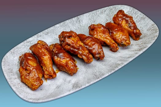 Composition of a plate of chicken wings with barbecue sauce on a magenta and light blue gradient background